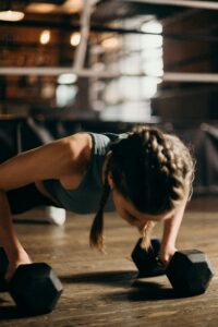 Fit woman doing push-ups with dumbbells indoors, emphasizing strength training and fitness.