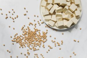 Flat lay of tofu cubes and soybeans scattered on a white marble surface, ideal for food photography.