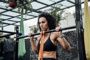 Woman exercising with pull-ups in an outdoor gym, surrounded by plants, showcasing fitness and healthy lifestyle.