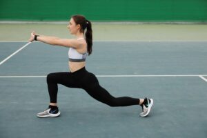 Woman in activewear stretching on a tennis court, focusing on fitness and flexibility.