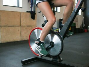 A woman cycling on a stationary bike indoors, focusing on fitness and leg muscle strength.